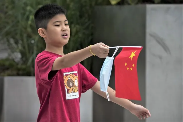 A kid hangs his face mask on a national flag as he walks on a street in Beijing, Tuesday, August 9, 2022. Chinese authorities have closed Tibet's famed Potala Palace after a minor outbreak of COVID-19 was reported in the Himalayan region. (Photo by Andy Wong/AP Photo)