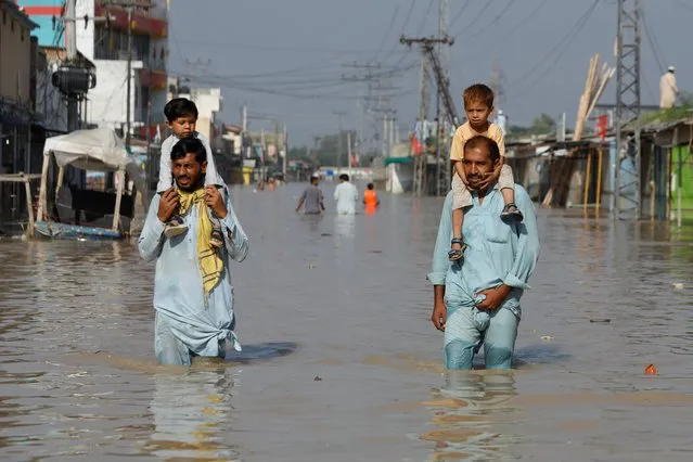Men carry children on their shoulders and wade along a flooded road, following rains and floods during the monsoon season in Nowshera, Pakistan on August 29, 2022. (Photo by Fayaz Aziz/Reuters)