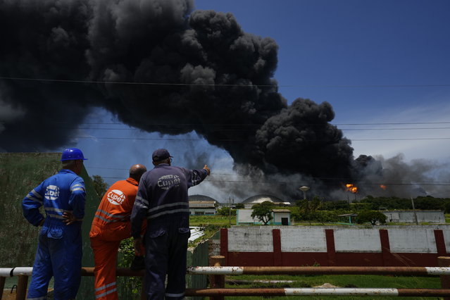 Workers of the Cuba Oil Union, known by the Spanish acronym CUPET, watch a huge rising plume of smoke from the Matanzas Supertanker Base, as firefighters work to quell a blaze which began during a thunderstorm the night before, in Matazanas, Cuba, Saturday, August 6, 2022. (Photo by Ramon Espinosa/AP Photo)