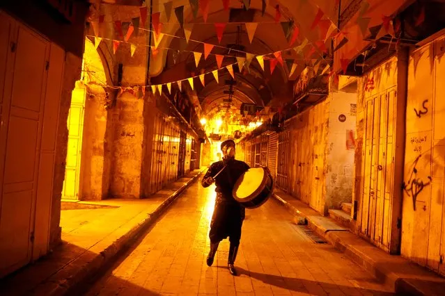 A Palestinian Musharati wearing a mask beats a drum to wake Muslims up to have the predawn meal before they start their long-day fast, during the holy month of Ramadan, amid concerns about the spread of the coronavirus disease (COVID-19), in Nablus, in the Israeli-occupied West Bank on April 28, 2020. (Photo by Raneen Sawafta/Reuters)