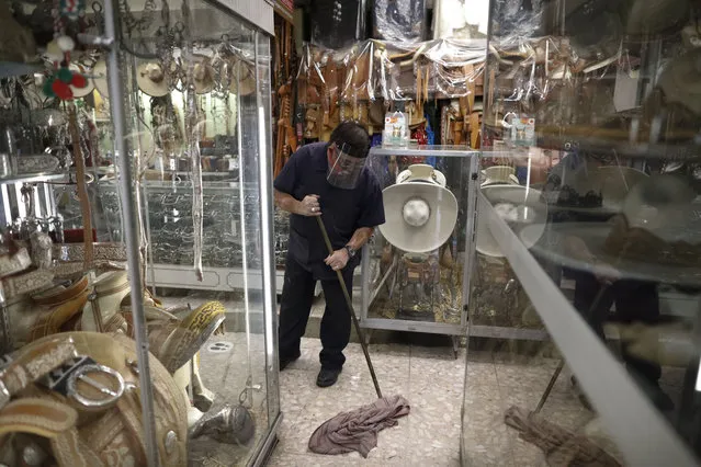 Employee Manuel Del Razo wears a mask and face shield as he mops inside Talabarteria, an equestrian and cowboy supply store that reopened today, in central Mexico City, Monday, July 6, 2020. After three months of shutdown, officials allowed a partial reopening of the downtown commercial area last week, although COVID-19 cases continue to climb. (Photo by Rebecca Blackwell/AP Photo)