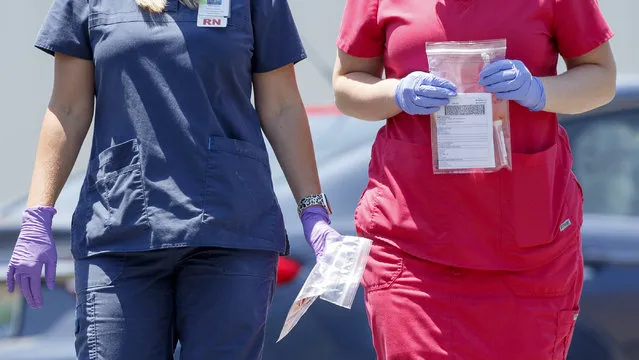 Nurse Melissa Bailey, left, and medical assistant Heather Andrews carry collected samples at DeKalb Regional Medical Center's drive thru COVID-19 testing site on Thursday, July 16, 2020 in Fort Payne, Ala. (Photo by C.B. Schmelter/Chattanooga Times Free Press via AP Photo)