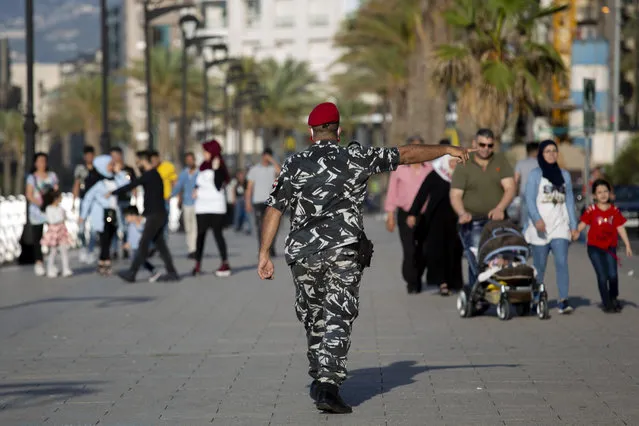 A policeman orders people to evacuate the Mediterranean Sea corniche during the first day of the Eid al-Fitr holiday, in Beirut, Lebanon, Sunday, May 24, 2020. Many among those walking on the boardwalk did not wear masks to stop the spread of the coronavirus and were ignoring social distancing rules, leading security forces to intervene, detaining some and fining others. (Photo by Hassan Ammar/AP Photo)