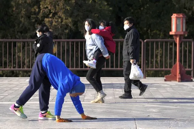 Visitors wearing masks watch as a resident walks on all four limbs as a form of exercise in the Temple of Heaven park in Beijing, Thursday, December 8, 2022. In a move that caught many by surprise, China announced a potentially major easing of its rigid “zero-COVID” restrictions, without formally abandoning the policy altogether. (Photo by Ng Han Guan/AP Photo)