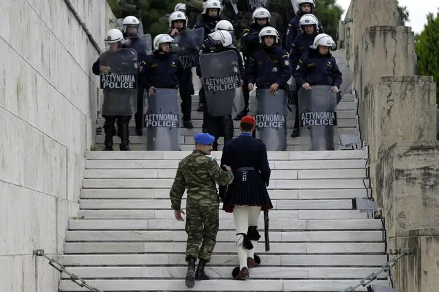 A military officer helps a Presidential Guard or Evzonas to move from his position as protesters approach the Tomb of the Unknown Soldier outside the Greek Parliament during a rally organized by Civil Servants' union in Athens, Monday, January 15, 2018. Athenians are without public transport for the day and services nationwide face disruptions as Greek labor unions strike to protest further creditor-demanded measures due to be voted in Parliament. (Photo by Thanassis Stavrakis/AP Photo)