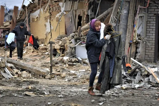 Local residents carry their belongings as they leave their home ruined in the Saturday Russian rocket attack in Zaporizhzhya, Ukraine, Sunday, January 1, 2023. (Photo by Andriy Andriyenko/AP Photo)
