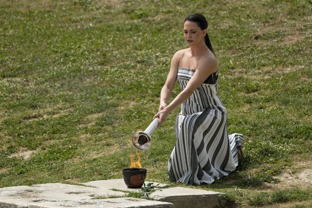Actress Mary Mina, playing high priestess, lights a torch from a flame lit the day before during the official ceremony of the flame lighting for the Paris Olympics, at the Ancient Olympia site, Greece, Tuesday, April 16, 2024. Cloudy skies prevented the traditional lighting, when an actress dressed as an ancient Greek priestess uses the sun to ignite a silver torch. Instead, a backup flame was used that had been lit on the same spot Monday, during the final rehearsal. (Photo by Petros Giannakouris/AP Photo)