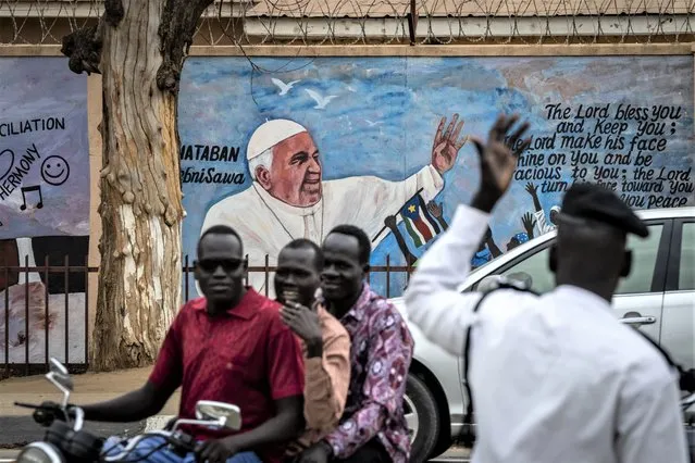 A traffic police officer standing in front of a mural of Pope Francis on the wall of a church directs motorcycles and other vehicles to get off the road as a convoy of government vehicles passes, on a street in the capital Juba, South Sudan Thursday, February 2, 2023. Pope Francis is due to travel to South Sudan later this week on the second leg of a six-day trip that started in Congo, hoping to bring comfort and encouragement to two countries that have been riven by poverty, conflicts and what he calls a “colonialist mentality” that has exploited Africa for centuries. (Photo by Ben Curtis/AP Photo)