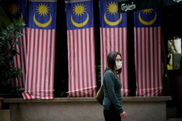 A woman wearing a face mask to help curb the spread of the coronavirus crosses a street with national flags on display to celebrate Malaysia Day in Kuala Lumpur, Malaysia, Wednesday, September 16, 2020. Malaysia Day is a public holiday held on September 16 every year to commemorate the establishment of the Malaysian federation on the same date in 1963. (Photo by Vincent Thian/AP Photo)
