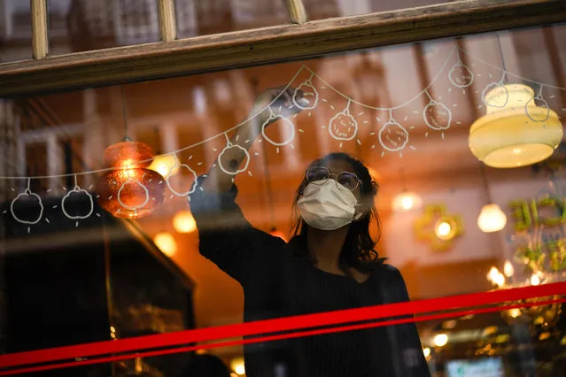 Graphic designer Chloe Vanhoecke, wearing a face mask to prevent the spread of the coronavirus COVID-19, works on Christmas decorations in a restaurant window in downtown Brussels, Wednesday, December 2, 2020. In Belgium, experts say wearing masks and practicing social distancing will be essential in containing the spreading of the virus when shopping returns to a sense of normalcy. (Photo by Francisco Seco/AP Photo)