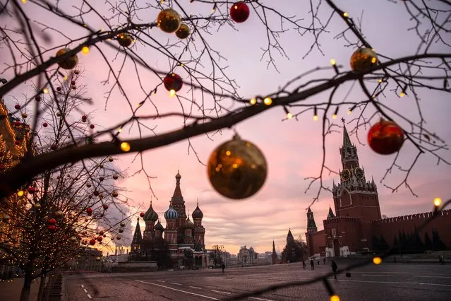 Balls and lights are seen on trees decorated for Christmas and New Year celebrations during a sunrise over Red Square, with St. Basil Cathedral and the Spasskaya Tower, right, in the background in Moscow, Russia, Saturday, December 12, 2020. (Photo by Pavel Golovkin/AP Photo)