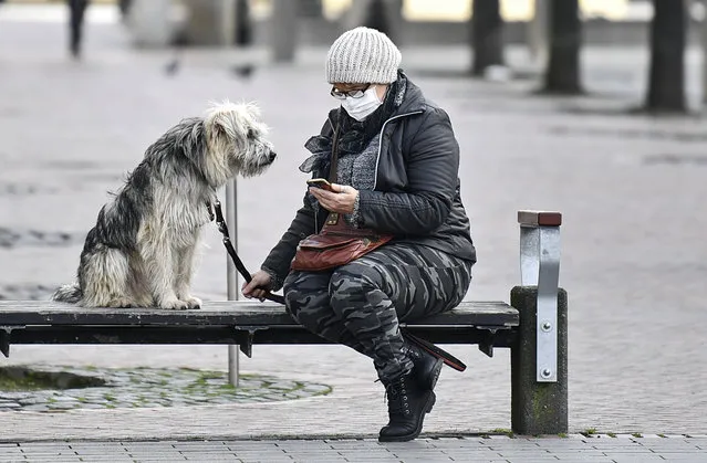A woman with a face mask and a dog sit on a bench at the almost abandoned downtown in Duisburg, Germany, Monday, January 25, 2021. (Photo by Martin Meissner/AP Photo)
