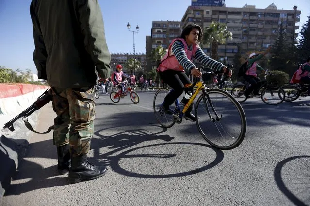 People cycle past a Syrian Army soldier along a street during a biking tour for charity, in Damascus December 11, 2015. (Photo by Omar Sanadiki/Reuters)