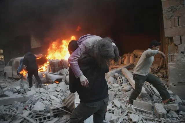 A man carries an injured child amidst rubble near a burning vehicle in a site damaged from what activists said was shelling by forces loyal to Syria's President Bashar al-Assad in the town of Douma, eastern Ghouta in Damascus, Syria December 30, 2015. (Photo by Bassam Khabieh/Reuters)