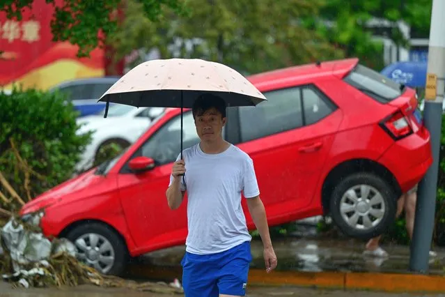 A man walks past a damaged car along a street, after heavy rains in Mentougou district in Beijing on July 31, 2023. Heavy rains battered northern China on July 31, killing at least two people in Beijing while washing away cars and inundating subway stations, with the capital issuing its highest alerts for flooding and landslides. (Photo by Pedro Pardo/AFP Photo)