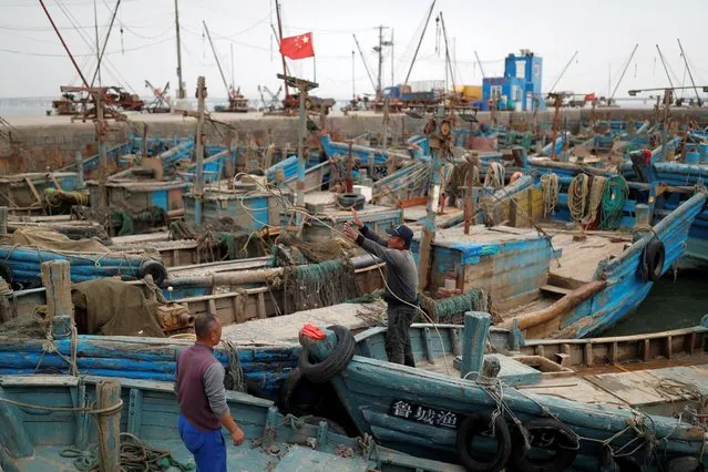 Fishermen stand on boats at a wharf on the coast of Qingdao, Shandong province, China, following an oil spill in the Yellow Sea caused by a collision between tanker A Symphony and bulk vessel Sea Justice off Qingdao port, April 28, 2021. (Photo by Carlos Garcia Rawlins/Reuters)