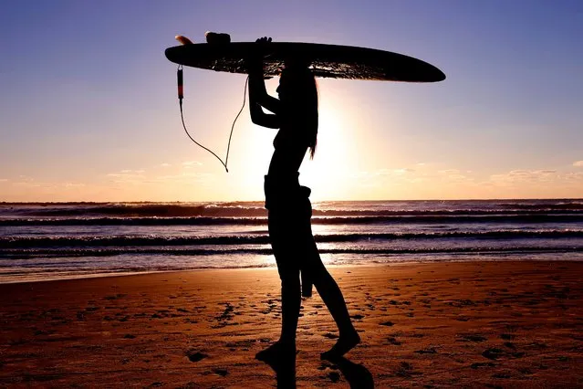 An Israeli surfer carries her board at sunset on the shore of the coastal city of Netanya, north of Tel Aviv, on January 21, 2021, during a nationwide lockdown after a spike in COVID-19 cases. (Photo by Jack Guez/AFP Photo)