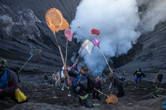 People try to catch offerings thrown by Tengger tribe people off the summit of the active Mount Bromo volcano in Probolinggo, East Java province on June 26, 2021, during the Yadnya Kasada festival to seek blessings from the main deity by presenting offerings of rice, fruit, livestock and other items. (Photo by Juni Kriswanto/AFP Photo)