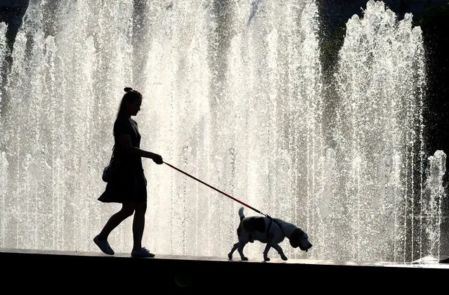 A woman walks a dog past a fountain near Finland railway station in St Petersburg, Russia on July 10, 2021. (Photo by Peter Kovalev/TASS)