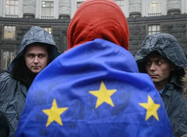 A protester wrapped in a EU flag attends a rally to support EU integration as police stand guard in front of the Ukrainian cabinet of ministers building in Kiev November 25, 2013. (Photo by Gleb Garanich/Reuters)
