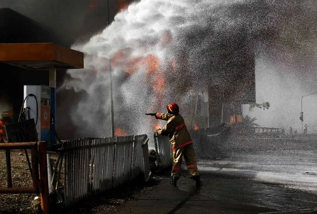 A firefighter standing near a Conoil petrol filing station directs his colleagues as to which direction to apply their hose, during a fire opposite the Nigeria National Petroleum corporation headquarters in Abuja, Nigeria, on December 5, 2013. (Photo by Afolabi Sotunde/Reuters)
