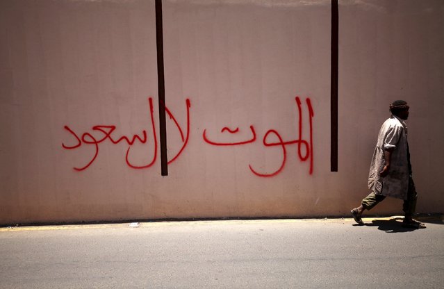 A man walks past writting on a wall along a street damaged by an air strike on Monday that hit a nearby army weapons depot, in Sanaa April 21, 2015. The writting reads, “Death to Al-Saud”, referring to Saudi Arabia's royal family. (Photo by Mohamed al-Sayaghi/Reuters)