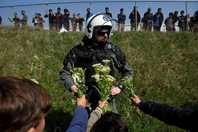 Migrant children offer flowers to a riot police officer next to a camp in the town of Diavata in northern Greece, April 4, 2019. (Photo by Alexandros Avramidis/Reuters)