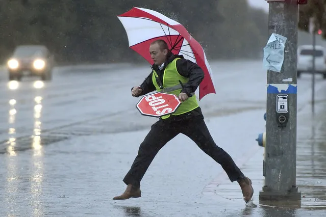 Garfield Elementary crossing guard Kai Dill tries to leap across the flooding street on Peach Ave., in Clovis, Calif., Monday, October 25, 2021. A massive storm barreled toward Southern California on Monday after flooding highways, toppling trees, cutting power to about 380,000 utility customers and causing rock slides and mud flows in areas burned bare by wildfires across the northern half of the state. (Photo by John Walker/Fresno Bee via AP Photo)