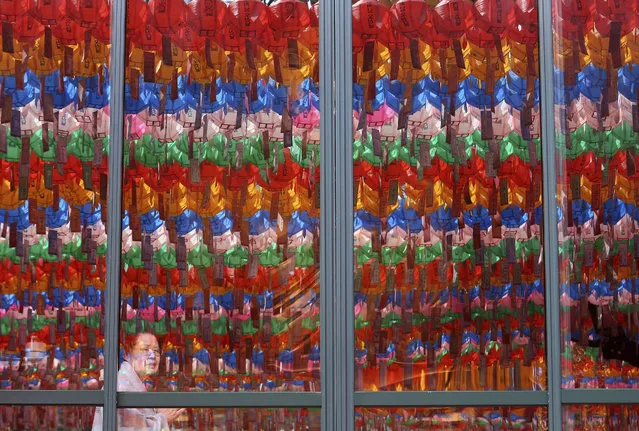 In this Tuesday, April 16, 2019, file photo, the lanterns decorated for upcoming celebration of Buddha's birthday on May 12 are reflected on the windows as a woman attends a service at Jogye temple in Seoul, South Korea. (Photo by Ahn Young-joo/AP Photo/File)