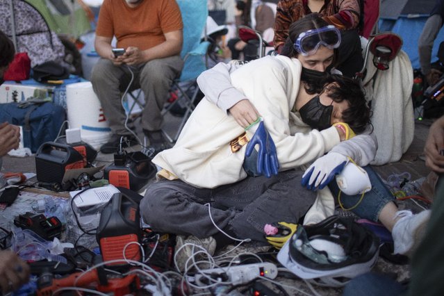 Pro-Palestinian demonstrators embrace while charging devices at an encampment on the UCLA campus Wednesday, May 1, 2024, in Los Angeles. (Photo by Ethan Swope/AP Photo)