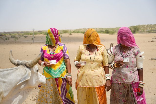 Women pose with their identity cards as they walk to cast their vote during the second phase of polling in the six-week long national election in the desert village Jaiisindhar, Barmer district, western Rajasthan state, India, Friday, April 26, 2024. (Photo by Deepak Sharma/AP Photo)