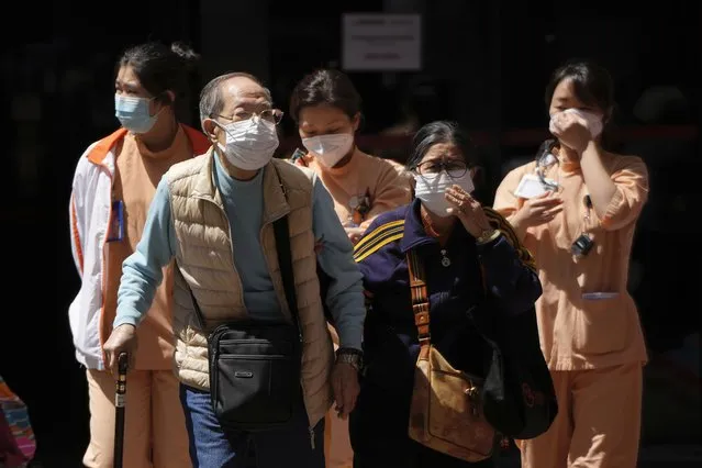 Elderly couple and medical staff walk out from the Queen Elizabeth Hospital in Hong Kong, Wednesday, March 9, 2022. Hong Kong leader Carrie Lam said Wednesday that there is “no specific time frame” for the testing exercise, as authorities focused their efforts on reducing the number of COVID-related deaths in the city during its worst outbreak to date. (Photo by Kin Cheung/AP Photo)