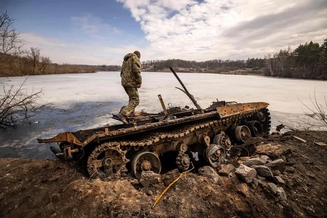 A Ukrainian serviceman stands near a destroyed Russian tank in the northeastern city of Trostianets, on March 29, 2022. Ukraine said on March 26, 2022 its forces had recaptured the town of Trostianets, near the Russian border, one of the first towns to fall under Moscow's control in its month-long invasion. (Photo by Fadel Senna/AFP Photo)