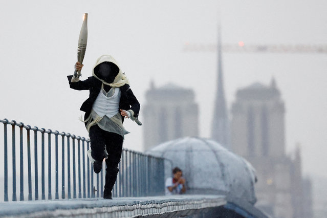 A torchbearer runs atop the Musee d'Orsay with the Notre-Dame-de-Paris cathedral in the background during the opening ceremony in Paris, France on July 26, 2024. (Photo by Peter Cziborra/Reuters)