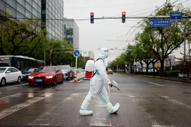 A worker wearing a protective suit and carrying disinfection equipment crosses a road amid the coronavirus disease (COVID-19) outbreak in Beijing, China on April 27, 2022. (Photo by Carlos Garcia Rawlins/Reuters)