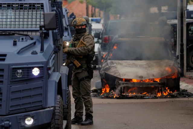 A special police forces officer stands next to a burning car, following clashes between Kosovo police and ethnic Serb protesters, who tried to prevent a newly-elected ethnic Albanian mayor from entering his office, in the town of Zvecan, Kosovo on May 26, 2023. (Photo by Valdrin Xhemaj/Reuters)