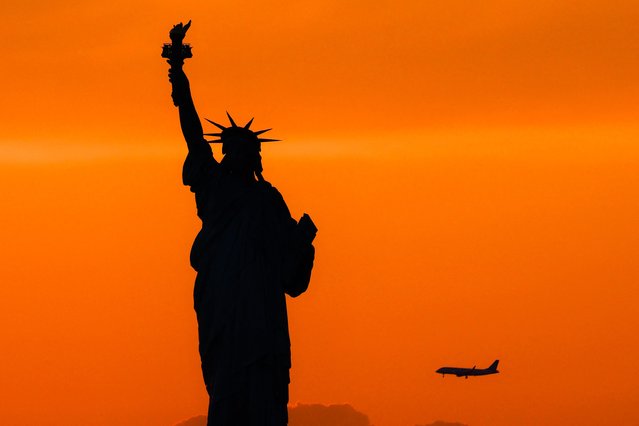 The Statue of Liberty is seen at dusk while a passenger aircraft approaches Newark airport in New York on August 11, 2024. (Photo by Charly Triballeau/AFP Photo)