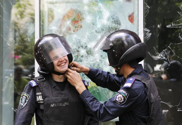 An Interior Ministry security force member assists his colleague to adjust the helmet as they stand guard outside a branch of Russian bank Sberbank which was attacked during a pro-Ukrainian anti-separatist rally in Kiev, June 22, 2014. (Photo by Valentyn Ogirenko/Reuters)