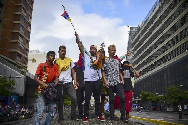 Opposition activists block an avenue during a protest in Caracas, on July 18, 2017. The Venezuelan opposition called for a 24- hour national civic strike next Thursday to pressure President Nicolas Maduro to withdraw the call to a National Constituent Assembly, after achieving a massive vote of rejection in a symbolic plebiscite. (Photo by Ronaldo Schemidt/AFP Photo)