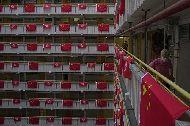 A resident walks besides the Chinese and Hong Kong flags hanging from a residential building to celebrate the 25th anniversary of Hong Kong handover to China, at a public housing estate, in Hong Kong, Saturday, June 25, 2022. As the former British colony marks the 25th anniversary of its return to China, reeling from pandemic curbs that devastated business and a crackdown on its pro-democracy movement, Hong Kong leaders say it is time to transform again and become a tech center that relies more on ties with nearby Chinese factory cities than on global trade. (Photo by Kin Cheung/AP Photo)