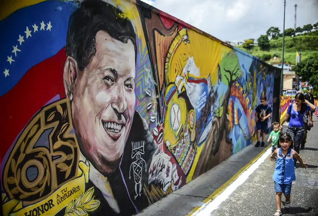 Children walk by a mural depicting late Venezuelan president Hugo Chavez at “23 de Enero” neighbourhood in Caracas near the "Cuartel de la Monta'a" museum where his body rests, on July 28, 2017 on the 63rd anniversary of his birth. The opposition called fresh nationwide demonstrations in defiance of a new government ban on rallies ahead of Sunday's controversial vote to elect a body to rewrite the constitution. (Photo by Ronaldo Schemidt/AFP Photo)