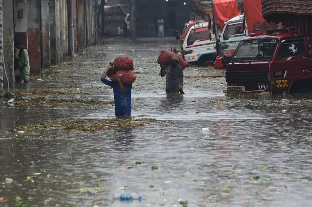 Labourers carry sacks of onions in a flooded market after a heavy rain shower in Lahore on July 14, 2022. (Photo by Arif Ali/AFP Photo)