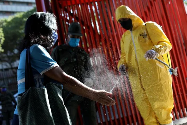 A worker wearing a protective suit disinfects a customer's hands at the entrance of a public market in response to the spread of coronavirus disease (COVID-19) in Caracas, Venezuela on March 18, 2020. (Photo by Manaure Quintero/Reuters)