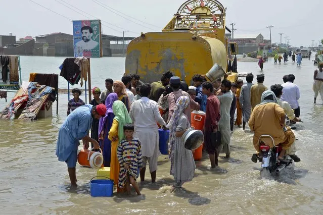 People jostle to get drinking water from a municipality water truck on a flooded road, in Sohbatpur, a district of Pakistan's southwestern Baluchistan province, Monday, August 29, 2022. (Photo by Zahid Hussain/AP Photo)