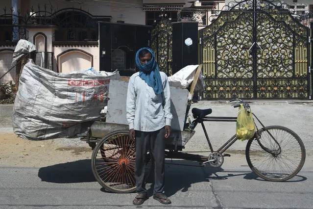 Ranjan Bind, 43, waste collector, poses for a picture in front of his bike cart in a residential colony during a government-imposed nationwide lockdown as a preventive measure against the COVID-19 coronavirus, in Faridabad, India, on April 22, 2020. Ahead of May Day on May 1, 2020, AFP portrayed 55 workers defying the novel coronavirus around the world. Ranjan works every day without a single day off. His only preventive measure against COVID-19 is to cover his face with a cloth. He said he works to earn a living and if given a choice, he would prefer to get paid and stay at home. (Photo by Money Sharma/AFP Photo)