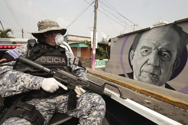 A National Civil Police Special Forces officer patrols past a mural of Armando Bukele, father of El Salvador's President Nayib Bukele, which was painted by supporters of the president outside a cultural center as a thank you gesture for creating the center when he was mayor, during the enforcement of the coronavirus-related quarantine, in the Iberia area of San Salvador, El Salvador, Thursday, April 23, 2020. When the coronavirus appeared, President Bukele closed the borders and airports and imposed a mandatory home quarantine for all except those working in the government, hospitals, pharmacies or other designated businesses. People were allowed out only to buy groceries, and violators were detained, with more than 2,000 being held for 30-day stints. (Photo by Salvador Melendez/AP Photo)