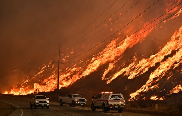 Emergency vehicles are on the side of the road as flames from the Hughes Fire race up the hill in Castaic, a northwestern neighborhood of Los Angeles, California, on January 22, 2025. A new wildfire erupted north of Los Angeles on January 22, exploding in size and sparking thousands of evacuation orders in a region already staggering from the effects of huge blazes. Ferocious flames were devouring hillsides near Castaic Lake, spreading rapidly to cover 5,000 acres (2,000 hectares) in just over two hours. The fire was being fanned by strong, dry Santa Ana winds that were racing through the area, pushing a vast pall of smoke and embers ahead of the flames. Evacuations were ordered for 19,000 people all around the lake, which sits around 35 miles north of Los Angeles, and close to the city of Santa Clarita. (Photo by Frederic J. Brown/AFP Photo)