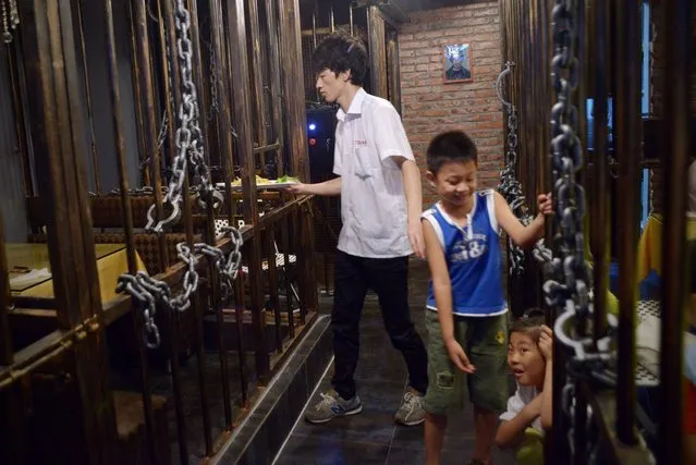 This picture taken on September 9, 2014 shows a waiter (L) handing over the food to customers (not in picture ) as two children play at a prison themed restaurant in Tianjin. (Photo by Wang Zhao/AFP Photo)