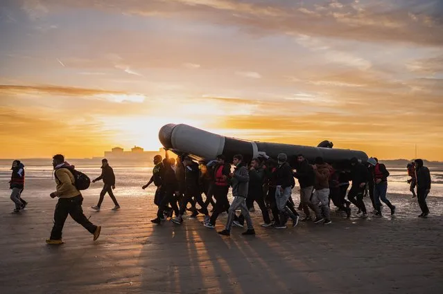 Migrants carry a smuggling boat on their shoulders as they prepare to embark on the beach of Gravelines, near Dunkirk, northern France on October 12, 2022, in a attempt to cross the English Channel. (Photo by Sameer Al-Doumy/AFP Photo)