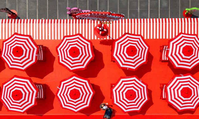 A woman pushes a baby-stroller past colourful beach umbrella installations outside a shopping mall in Bangkok on March 18, 2025. (Photo by Manan Vatsyayana/AFP Photo)